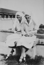 Long shot of two Nurses sitting outdoors on a low wall posing for the camera. Two Nurses, Circa 1940