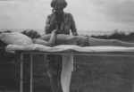 Medium shot taken outside, of a woman standing behind a cot where a patient lies. Visitor and Patient, Circa 1940