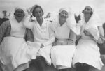Medium shot of four nurses seated in a row posing for the camera. Nurses, circa 1940