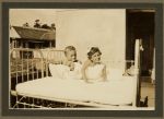 Medium shot of two children lying in a cot outdoors posing for the camera. Two Patients, Circa 1940