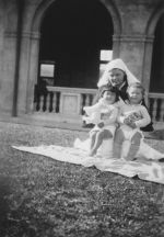 Medium shot of a kneeling Nurse holding two infants posing for the camera. Nurses and Children on the Lawn, Circa 1940