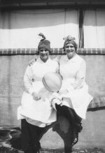 Medium shot of two medical staff seated on a low wall posing for the camera. Party Time, Circa 1940